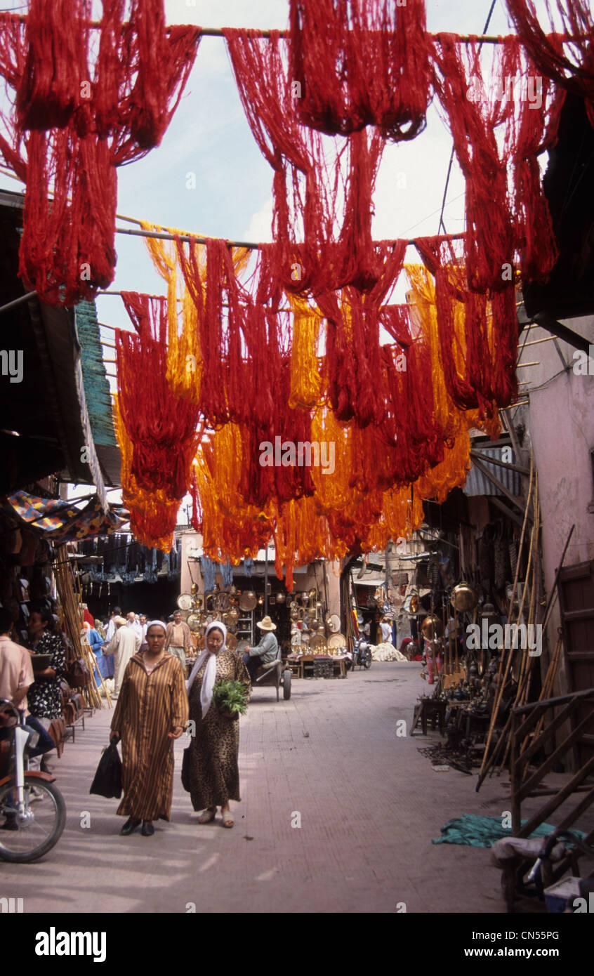 Due donne marocchine a piedi attraverso il bazaar di Marrakech e passando sotto i tessuti esposti , il Marocco. Foto Stock