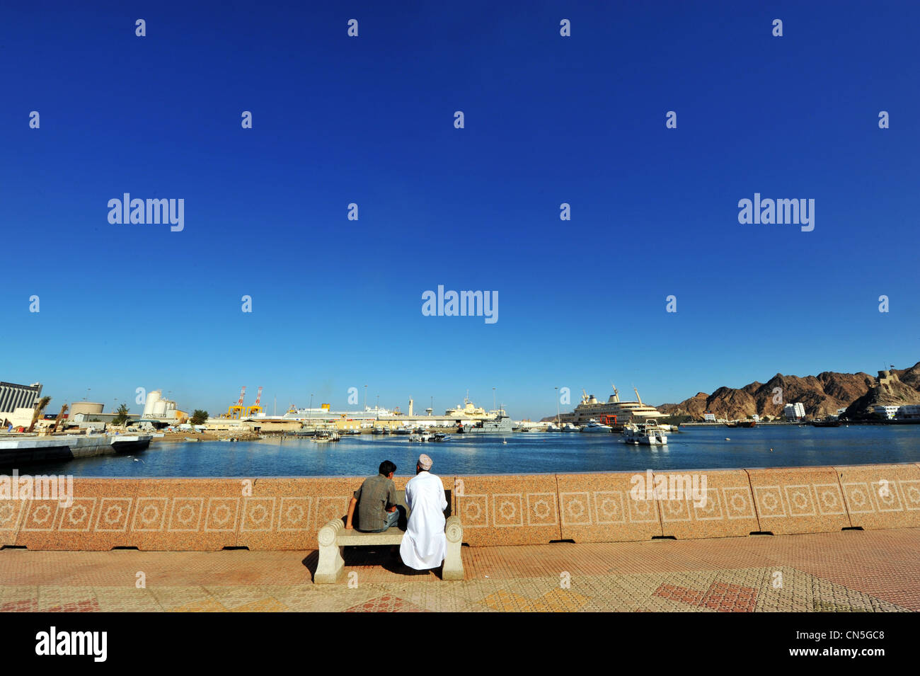 Il sultanato di Oman, Muscat Muttrah area portuale, Omani uomini seduti su una panchina pubblica sulla Corniche Foto Stock