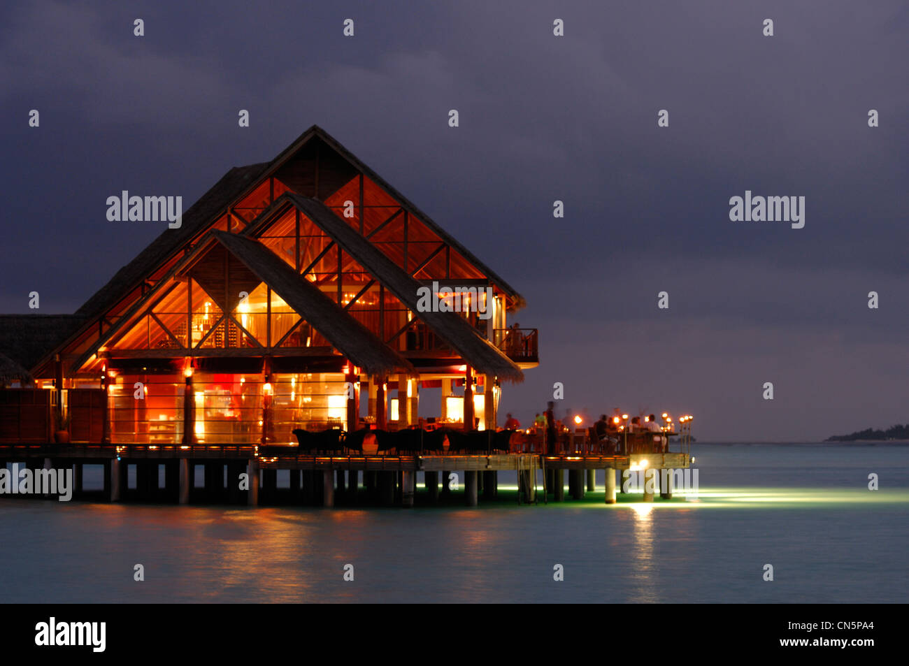 Maldive, South Male Atoll, Dhigu Island, Anantara Resort and Spa Hotel, tramonto dal mare su un ristorante su palafitte in Foto Stock