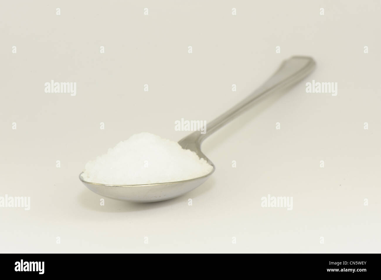 Cucchiaio contenente cristalli di sale preso su sfondo bianco Foto Stock