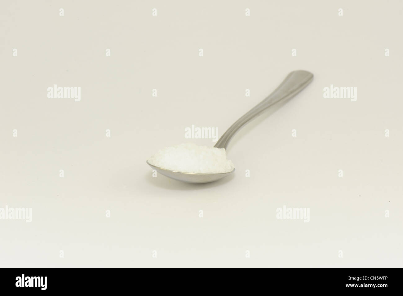 Cucchiaio contenente cristalli di sale preso su sfondo bianco Foto Stock