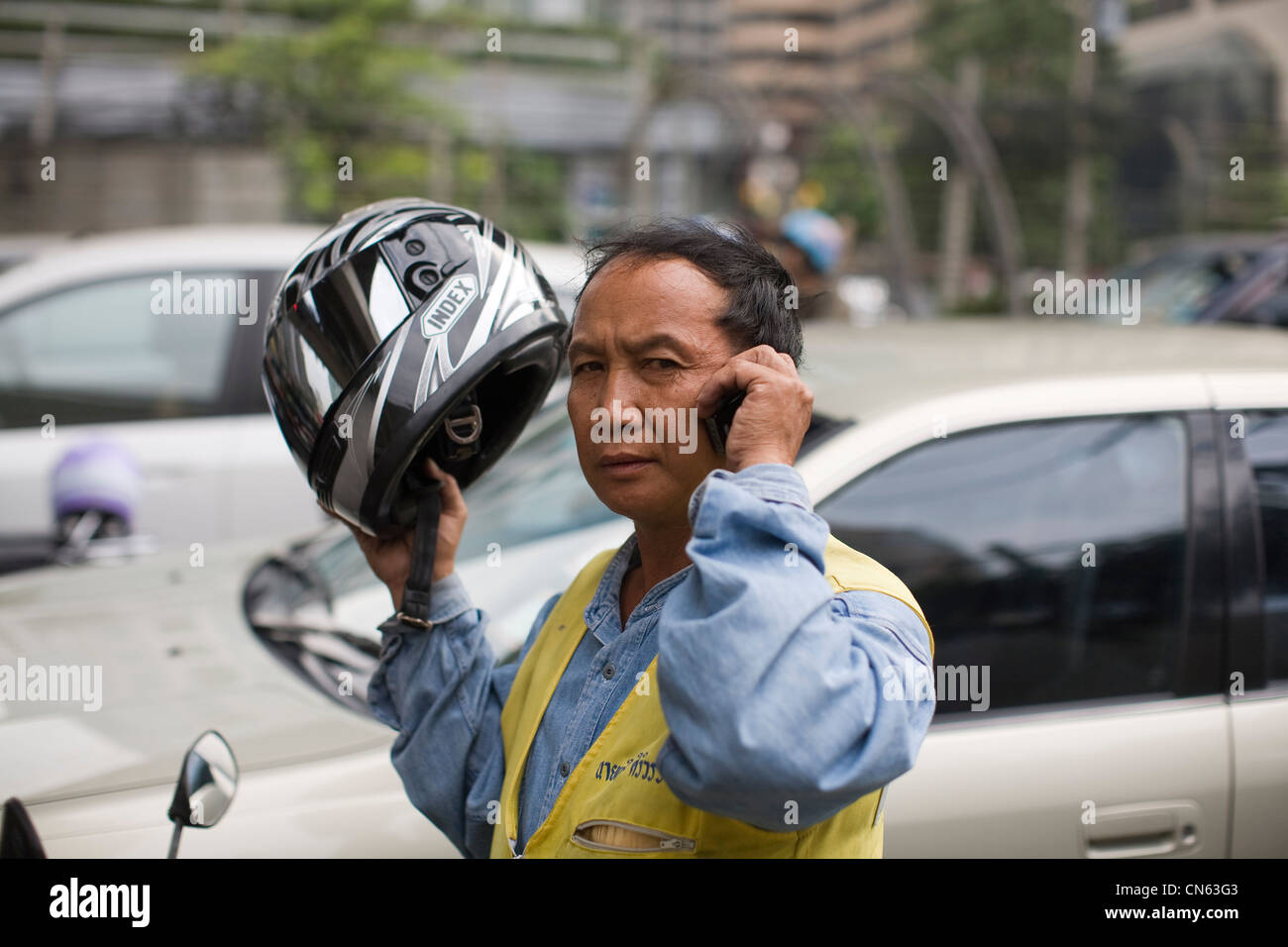 Un motocyclist rimuove il suo casco per rispondere al suo telefono cellulare, Bangkok, Thailandia Foto Stock