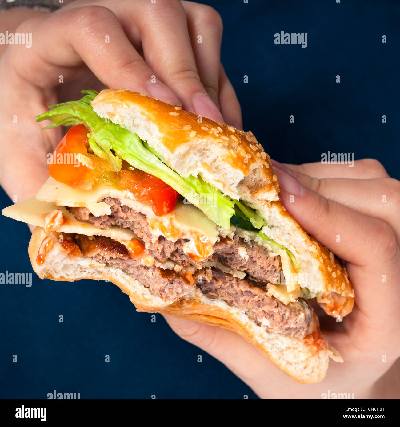 Close up di mani holding hamburger, su sfondo blu scuro. Foto Stock