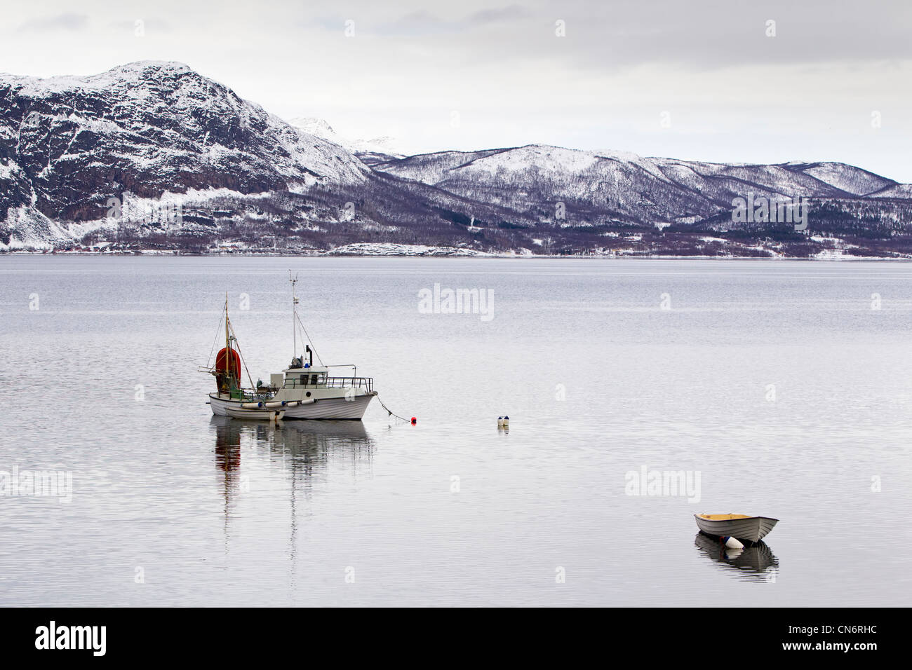 Una barca ormeggiata in un fiordo con montagne innevate nella distanza dietro Foto Stock
