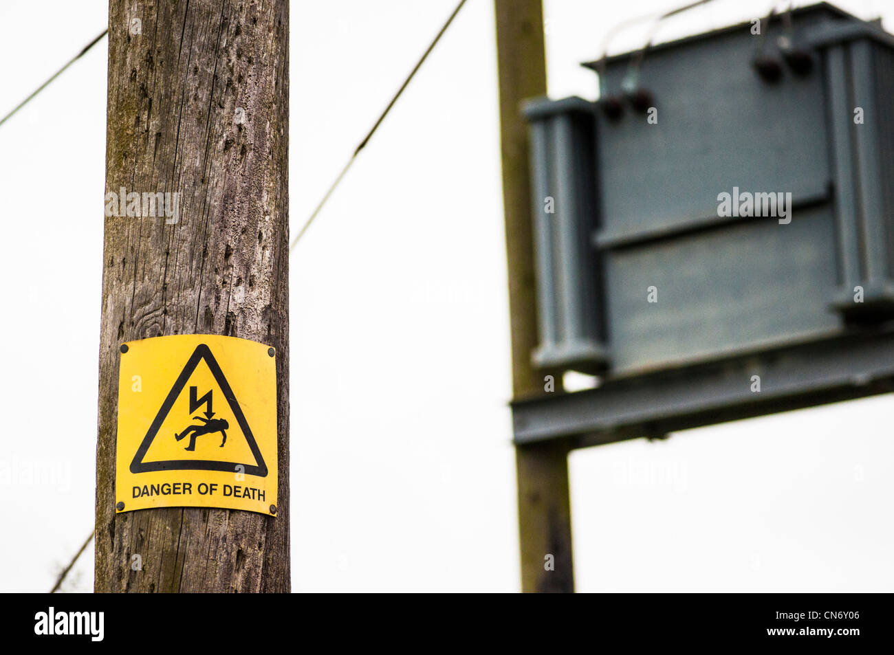 Pericolo di morte simbolo giallo di avvertimento su un palo del telegrafo, con l'elettricità la scatola di giunzione e cavi. Foto Stock