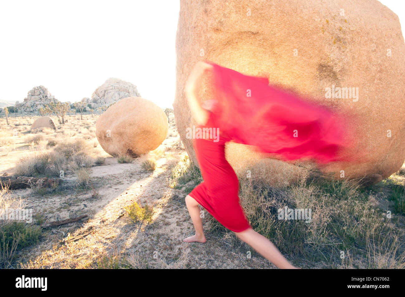 La donna in un ondata di rosso passione sfocata attraverso un paesaggio di pietra. Foto Stock