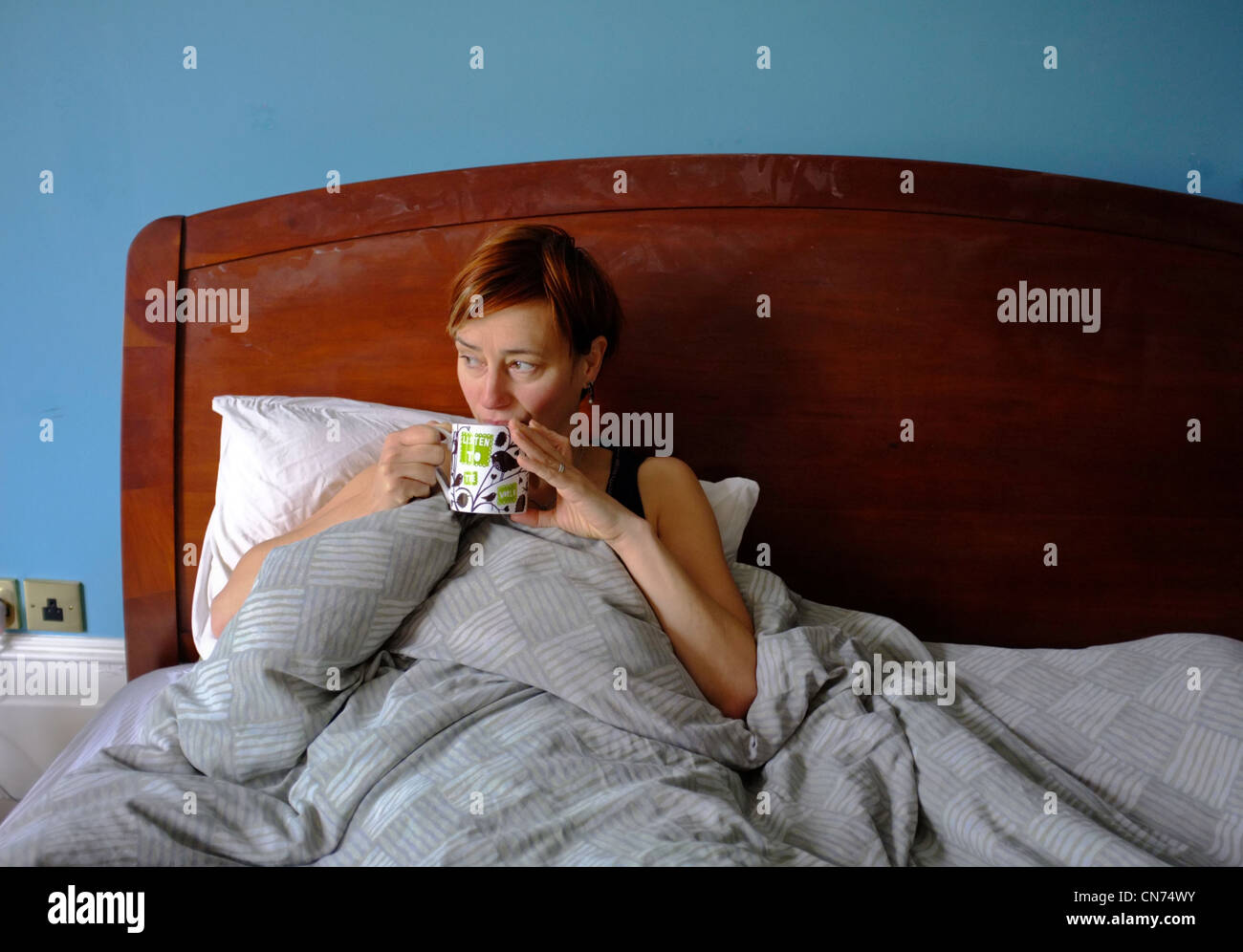 Una donna di mezza età bere il tè a letto Foto Stock