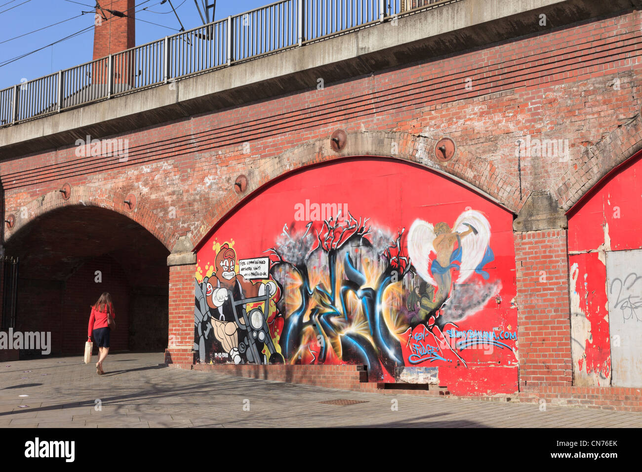 Scena urbana con la donna a piedi passato graffiti arte pittura sotto il vecchio ponte ferroviario archi. Leeds West Yorkshire England Regno Unito. Foto Stock