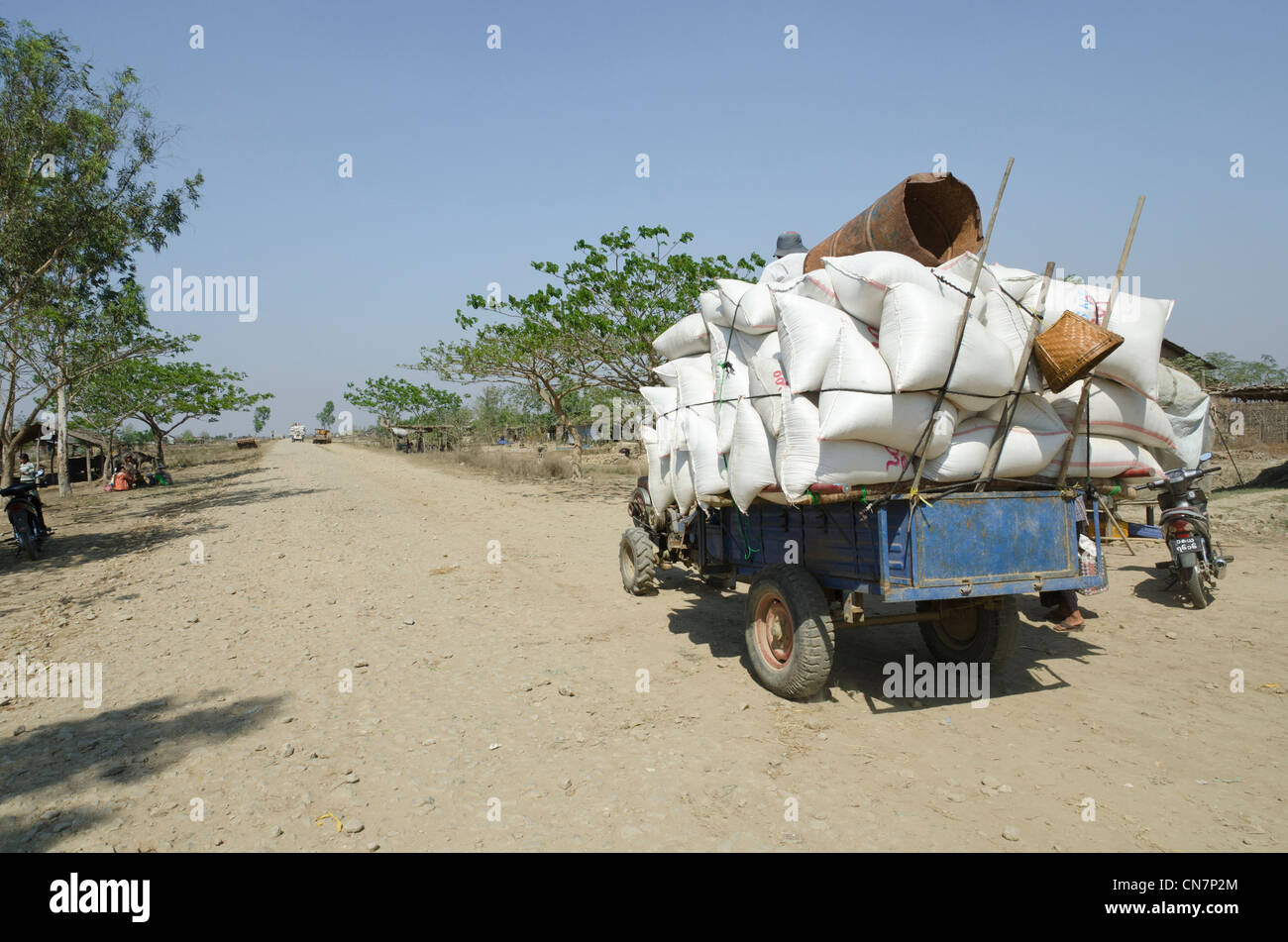 Trattore cinese il trasporto di sacchi di riso su strada sterrata. Delta di Irrawaddy. Myanmar. Foto Stock