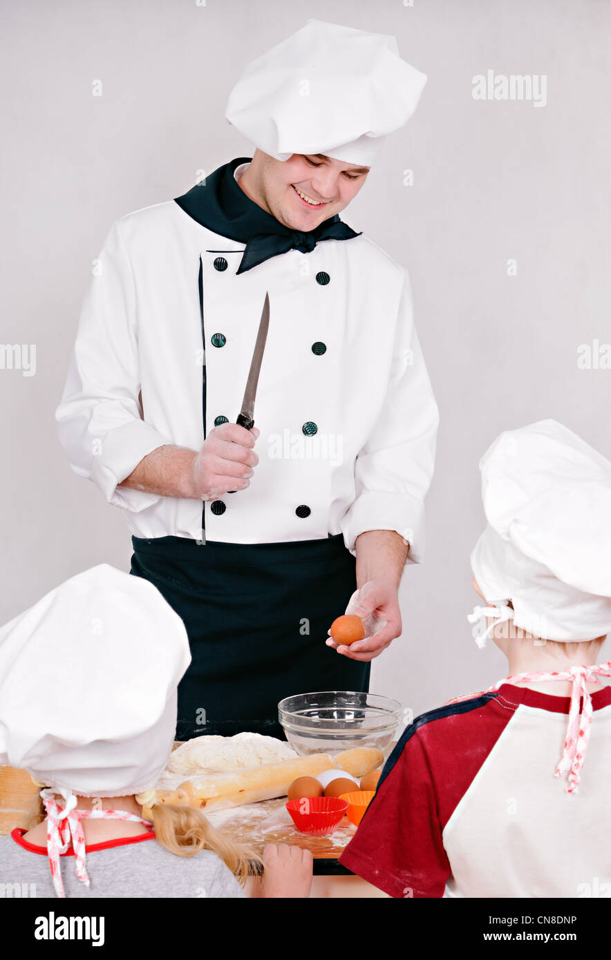 Lo chef è insegnare ai ragazzi a cuocere a fuoco lo sfondo grigio Foto Stock