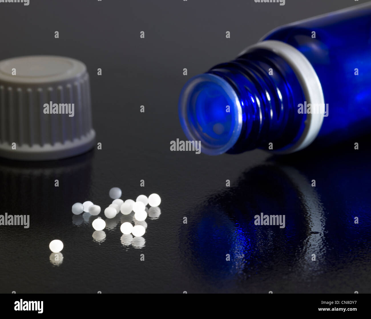 Aprire una piccola bottiglia di colore blu e il tappo sul buio massa riflettente con globuli intorno Foto Stock