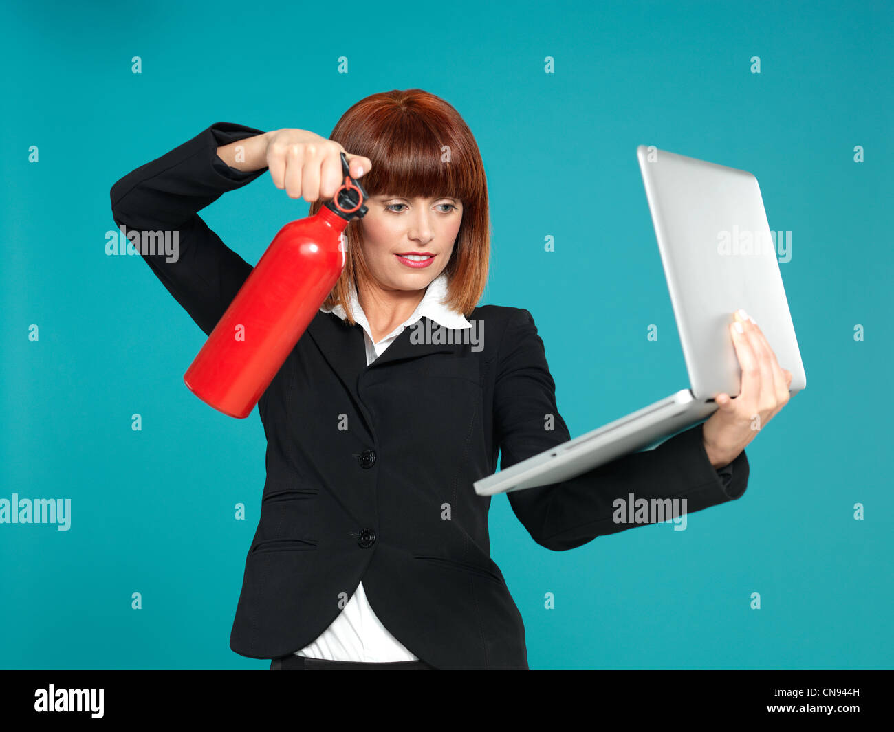 Divertente ritratto di una bella e giovane imprenditrice, utilizzando un estintore sul suo computer portatile, su sfondo blu Foto Stock