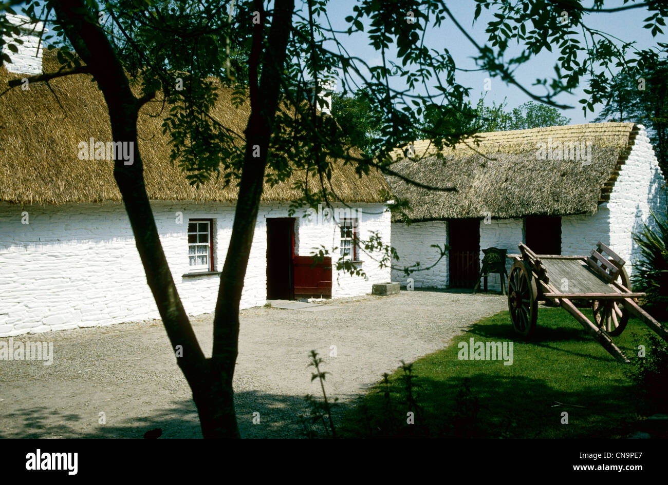 Periodo caratteristico con tetto di paglia di fattoria e cortile con un carrello in Irlanda Foto Stock