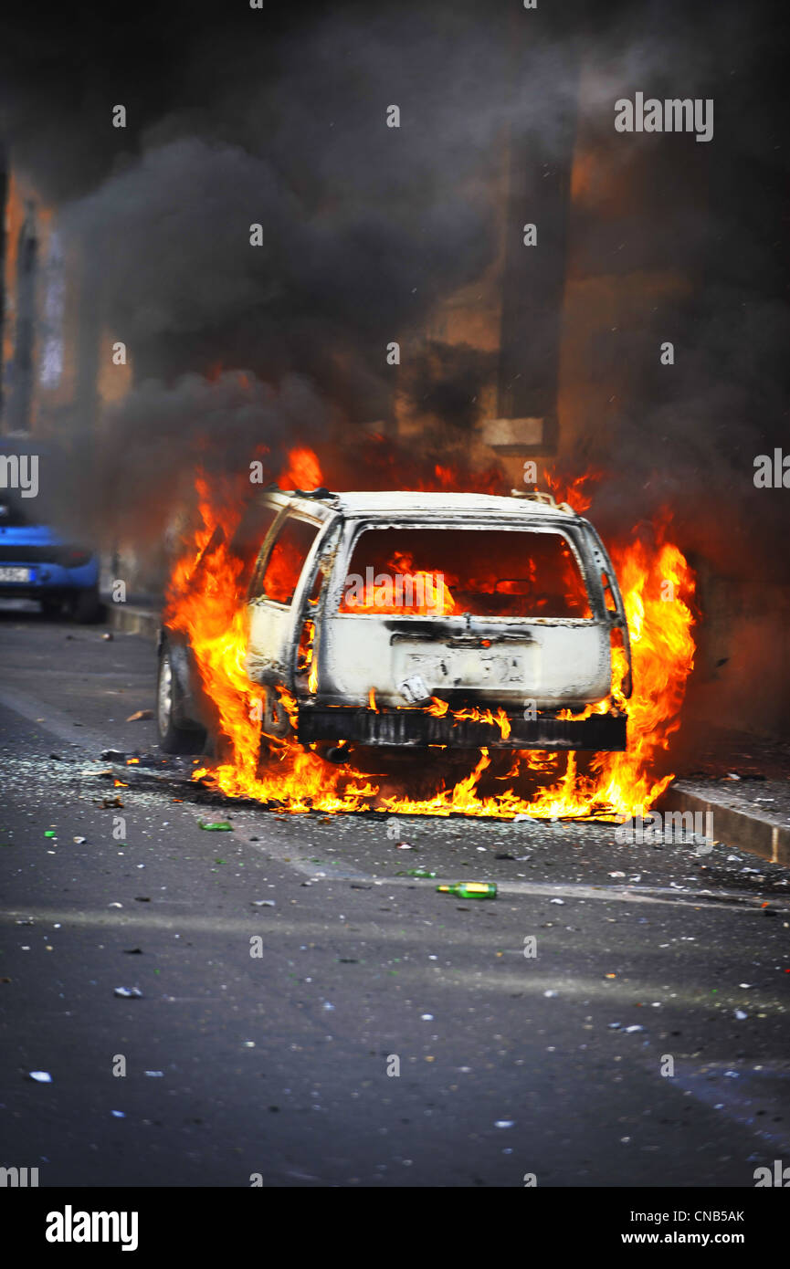 Scontri in strada - fiamme di fuoco salire dalla masterizzazione di un veicolo che è stato impostato dal variopinto rivoltosi sconosciuto in una strada della città durante le violenze in corso Foto Stock