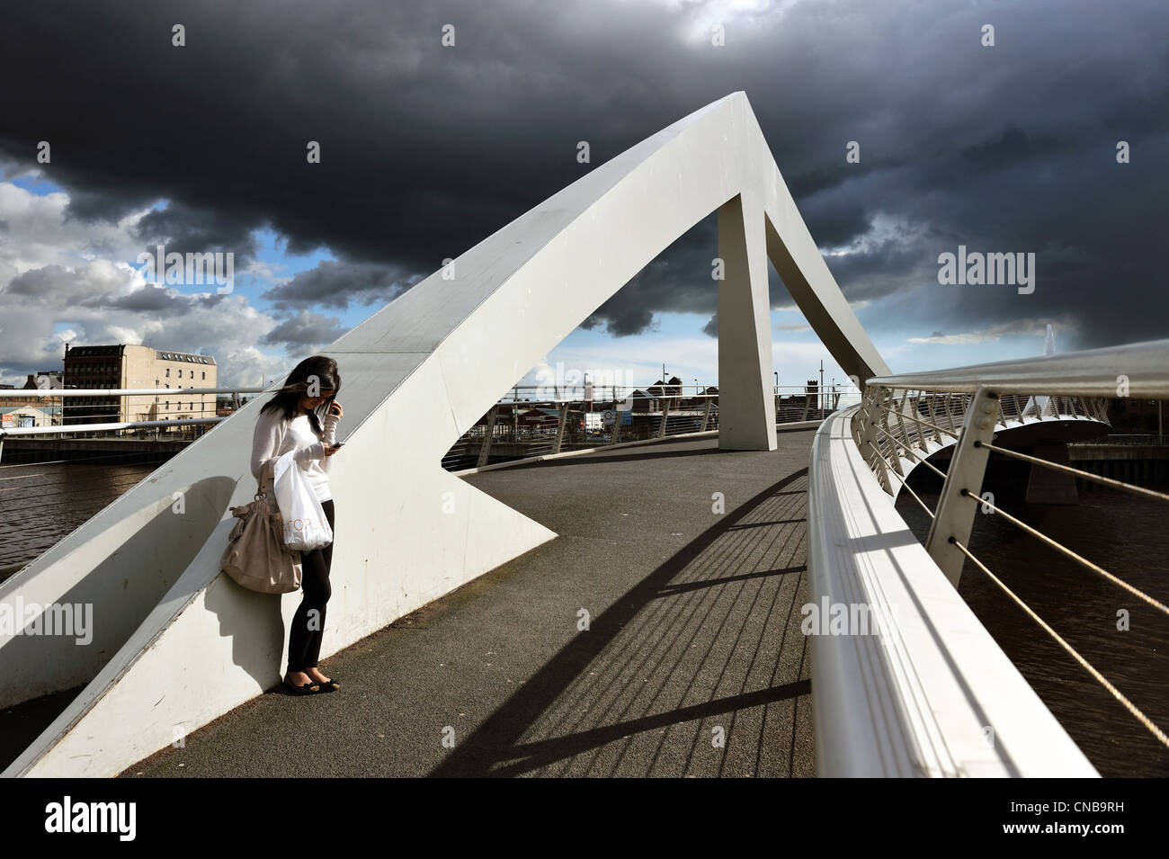 Una ragazza sorge il sole sulla sottolineatura ondulate Bridge (Ponte Broomielaw-Tradeston) come nuvole scure raccogliere nel cielo di Glasgow. Foto Stock