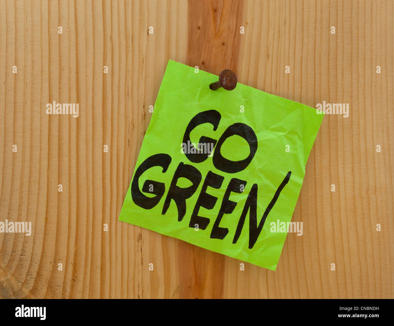 Go Green promemoria - accartocciata verde nota adesiva inchiodati in un asse di legno o a parete Foto Stock