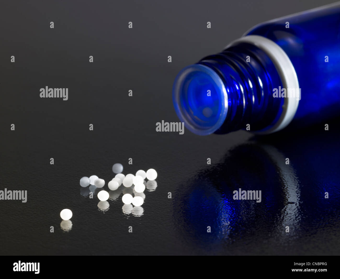 Dettaglio di aprire una piccola bottiglia di colore blu scuro sulla massa riflettente con globuli intorno Foto Stock