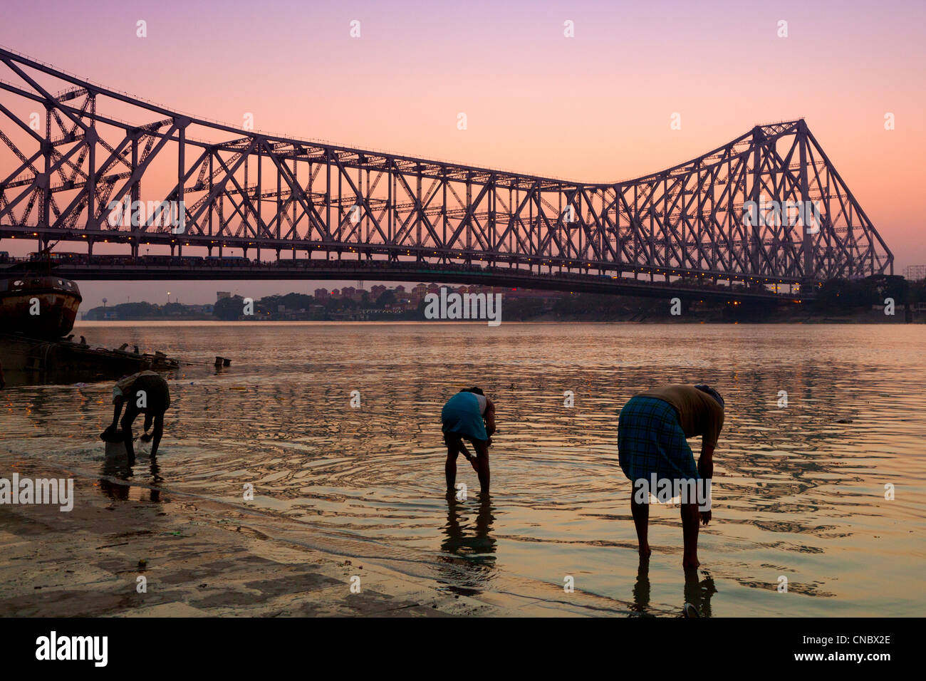 India Bengala Occidentale, Kolkata (Calcutta), la famiglia per la pulizia di utensili di cottura nel Fiume Hooghly con quella di Howrah ponte di sospensione Foto Stock