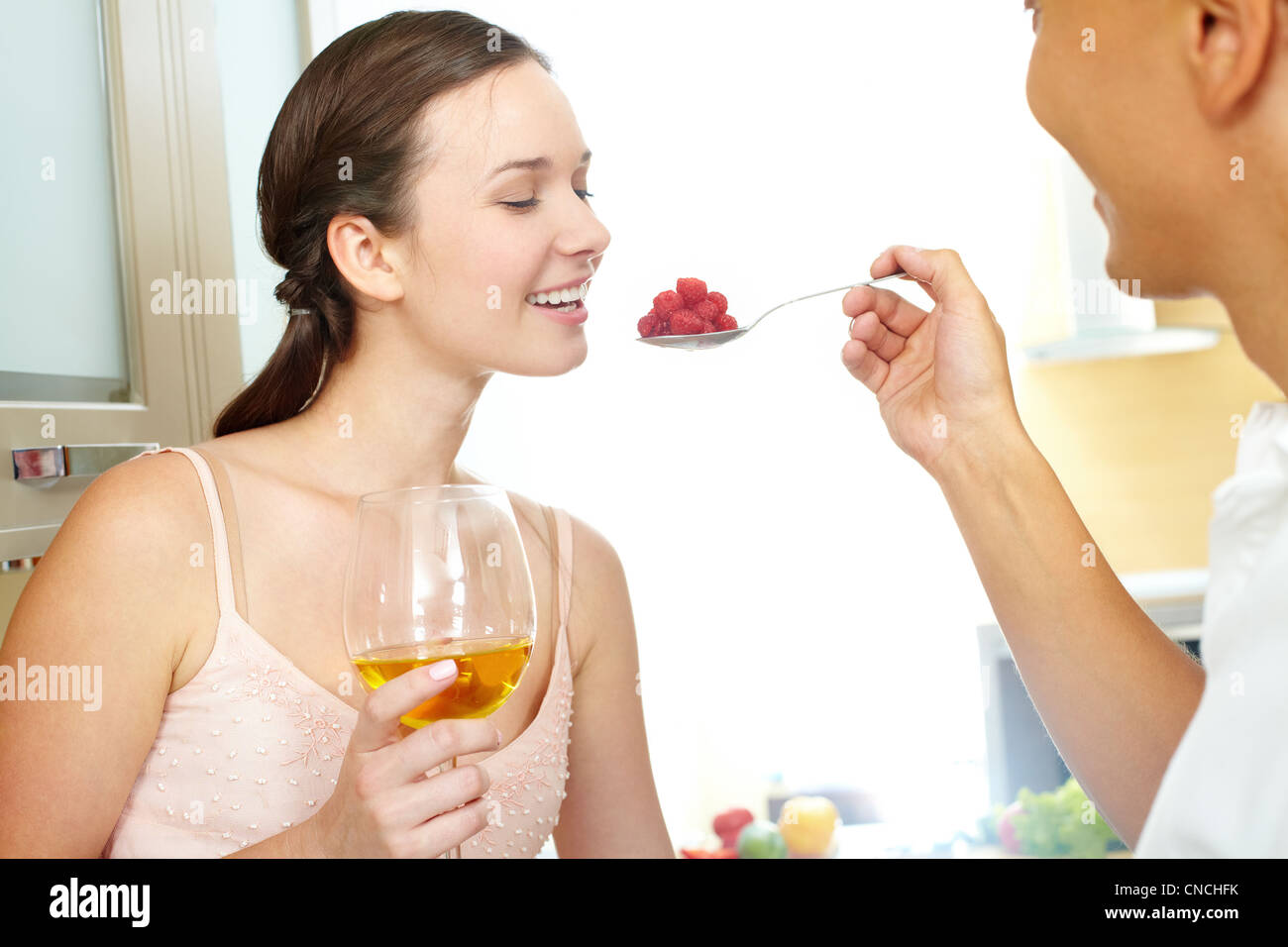 Immagine di donna felice con un bicchiere di vino guardando il cucchiaio di lamponi in suo marito mano Foto Stock