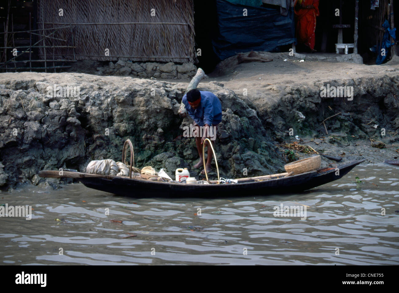 Un uomo si svuota una piccola barca sui beni in Bangladesh Foto Stock