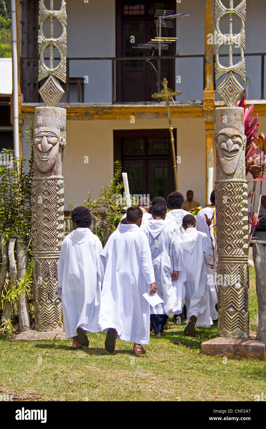 I chierichetti dopo la messa che porta una croce e immettendo un kanak house - Chiesa di Vao, Ile des Pins - Nuova Caledonia Foto Stock