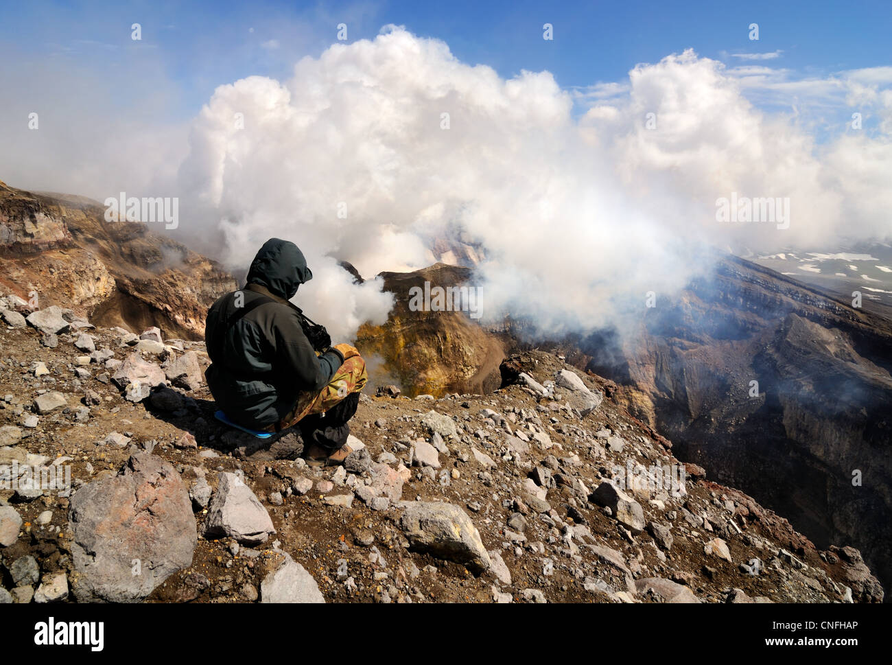 L'uomo sul bordo del vulcano Gorely cratere, guardando il gas e il pennacchio di vapore, penisola di Kamchatka, Russia Foto Stock