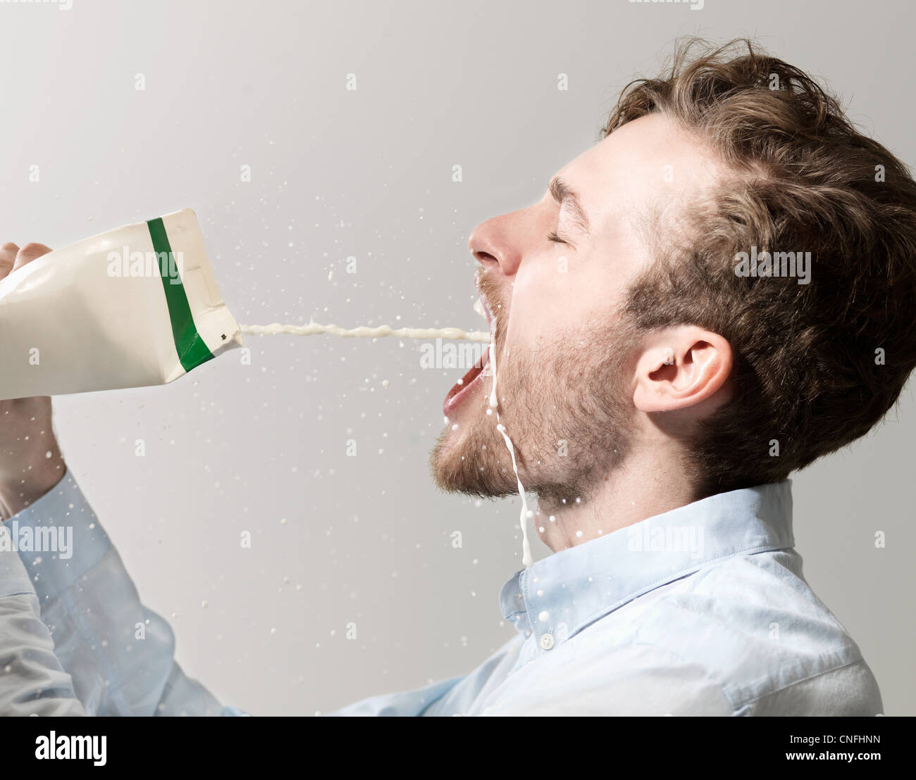 Giovane uomo fuoriuscita di latte dal cartone, studio shot Foto Stock