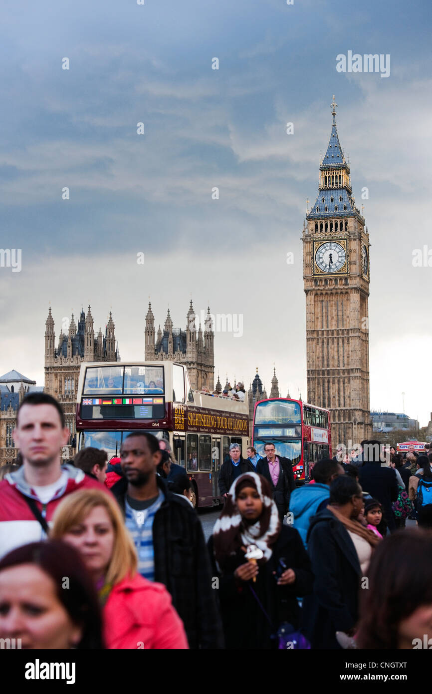 Turisti e pendolari camminando sul Westminster Bridge con il Big Ben e House of Commons in background e autobus turistici Foto Stock