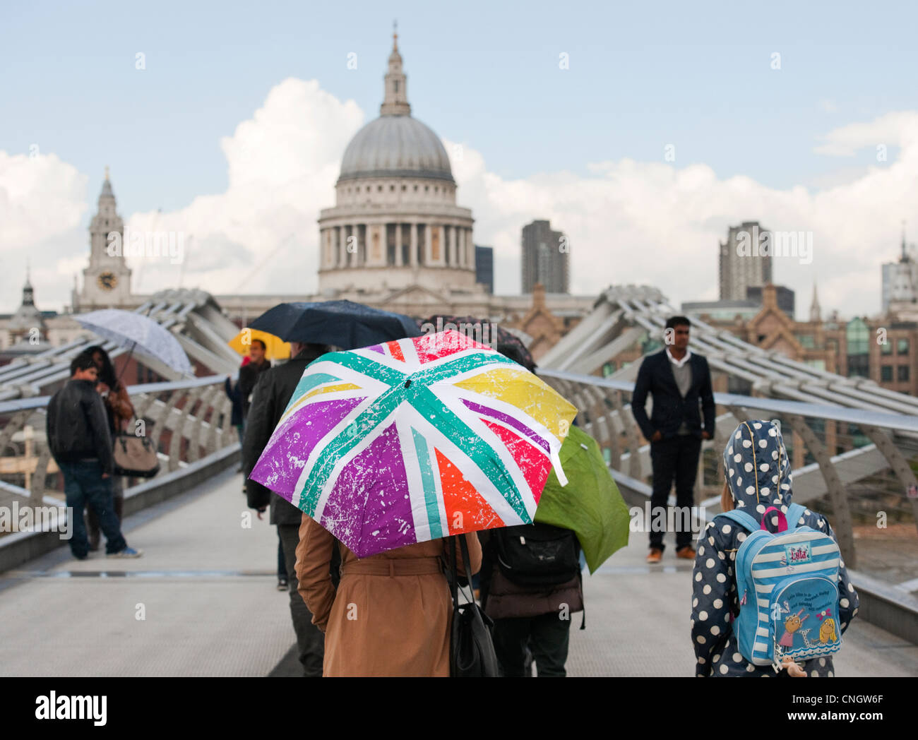 Famiglia con martoriata ombrello attraversando il Ponte del Millennio città di Londra verso la Cattedrale di St Paul Foto Stock