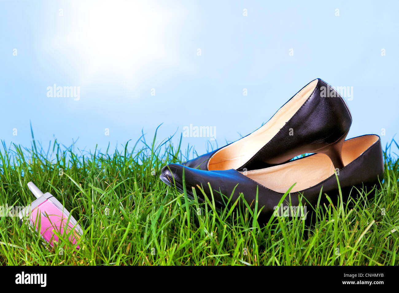 Foto di womens tacco alto scarpe e un telefono cellulare sull'erba contro un luminoso blu cielo con sole. Foto Stock