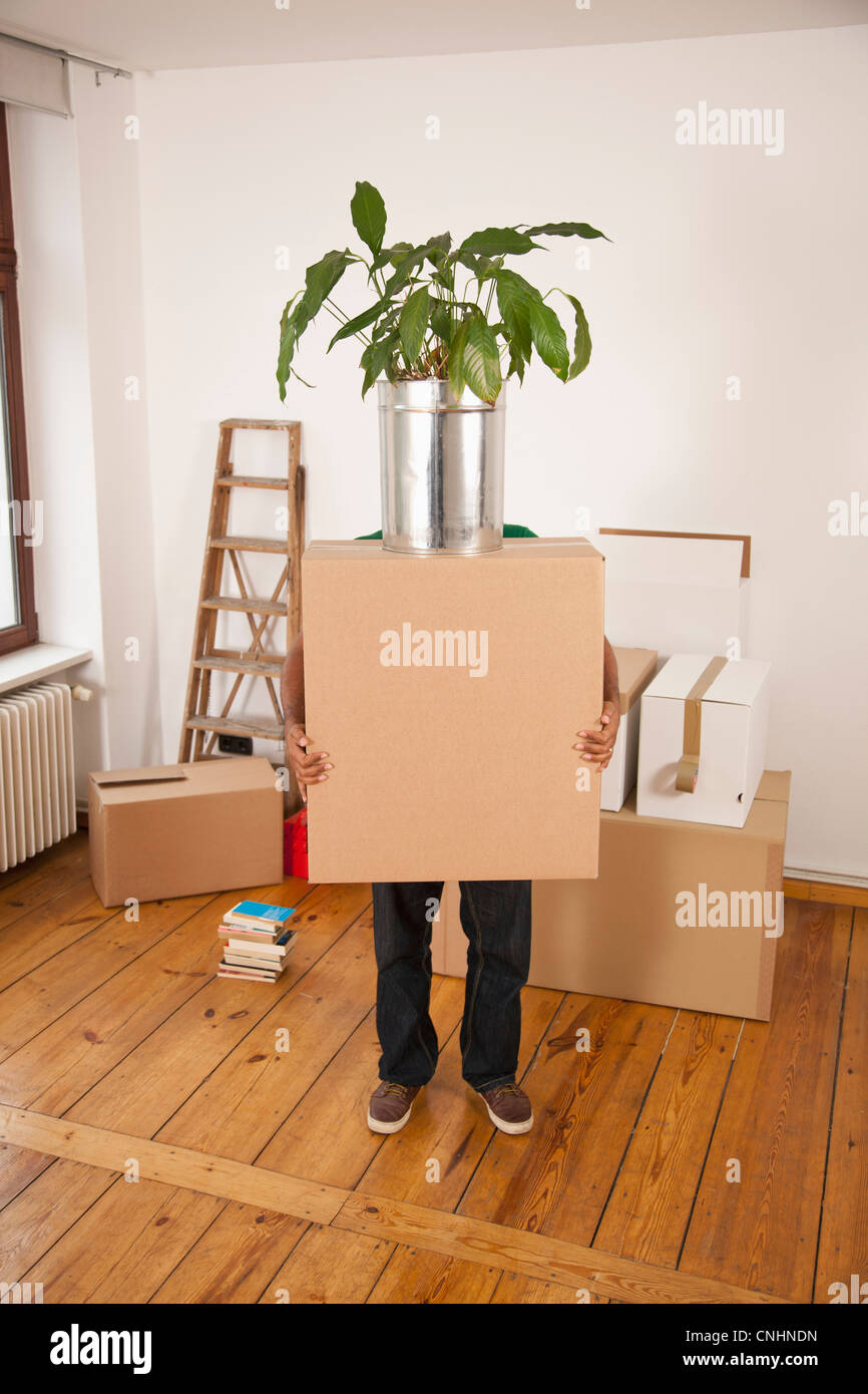 Un uomo che porta una scatola di movimentazione con un impianto in cima, faccia oscurata Foto Stock