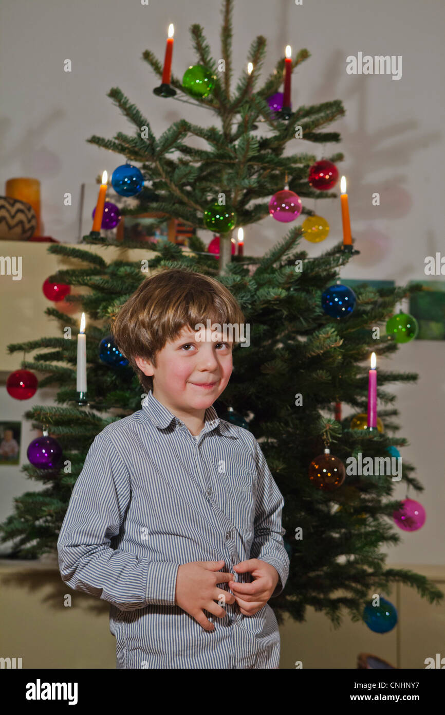 Un giovane ragazzo in piedi di fronte a un albero di Natale decorato Foto Stock