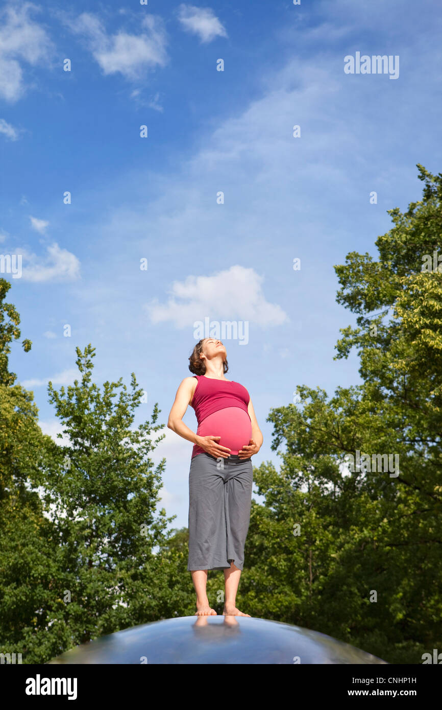 Una donna incinta in piedi in natura crogiolarsi al sole Foto Stock