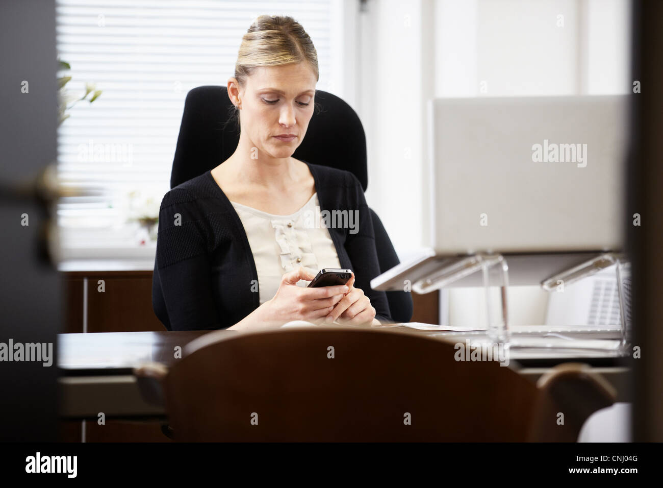 Imprenditrice alla scrivania, guardando il cellulare Foto Stock