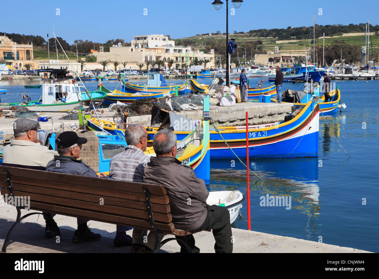 Gruppo di uomini anziani si affacciano sulle barche da pesca nel porto di Marsaxlokk, Malta, Europa Foto Stock