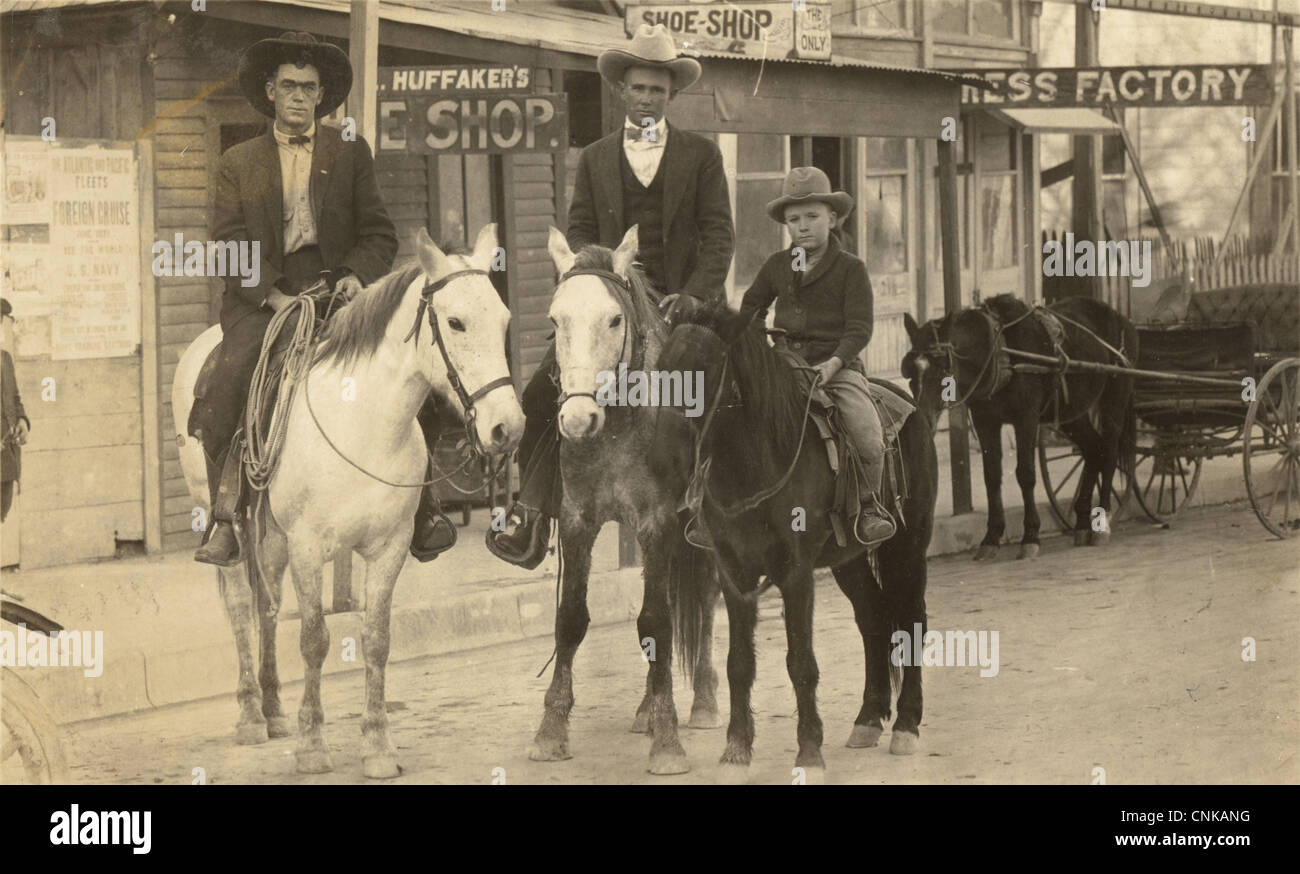 Due uomini & Boy a cavallo in città western Foto Stock