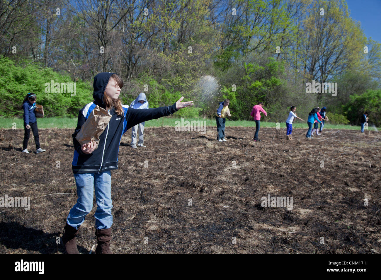 I bambini delle elementari seminare i semi per ripristinare la prateria nativi dopo che esso è stato intenzionalmente bruciata per eliminare le specie invasive. Foto Stock