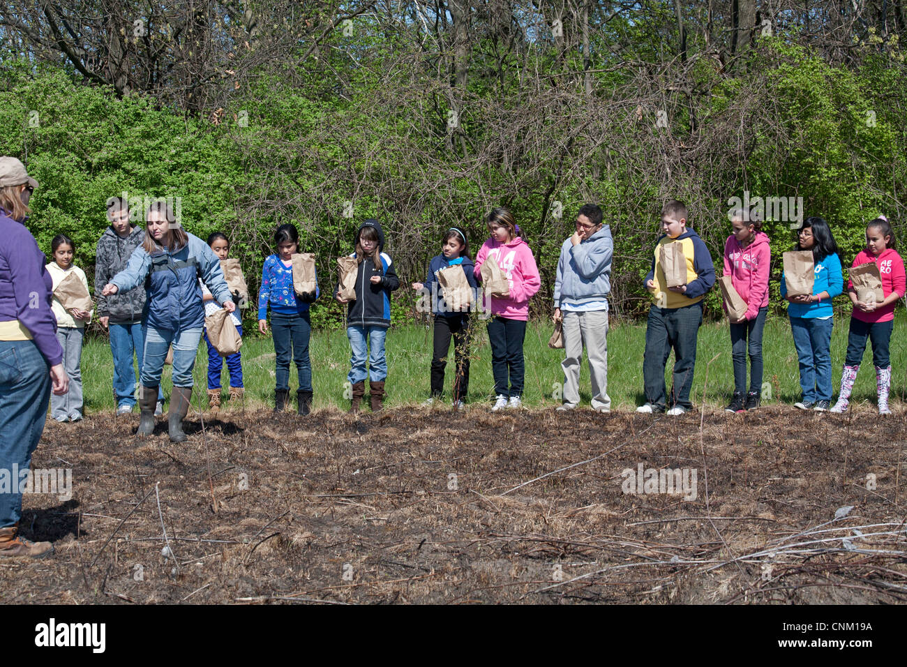 I bambini delle elementari seminare i semi per ripristinare la prateria nativi dopo che esso è stato intenzionalmente bruciata per eliminare le specie invasive. Foto Stock