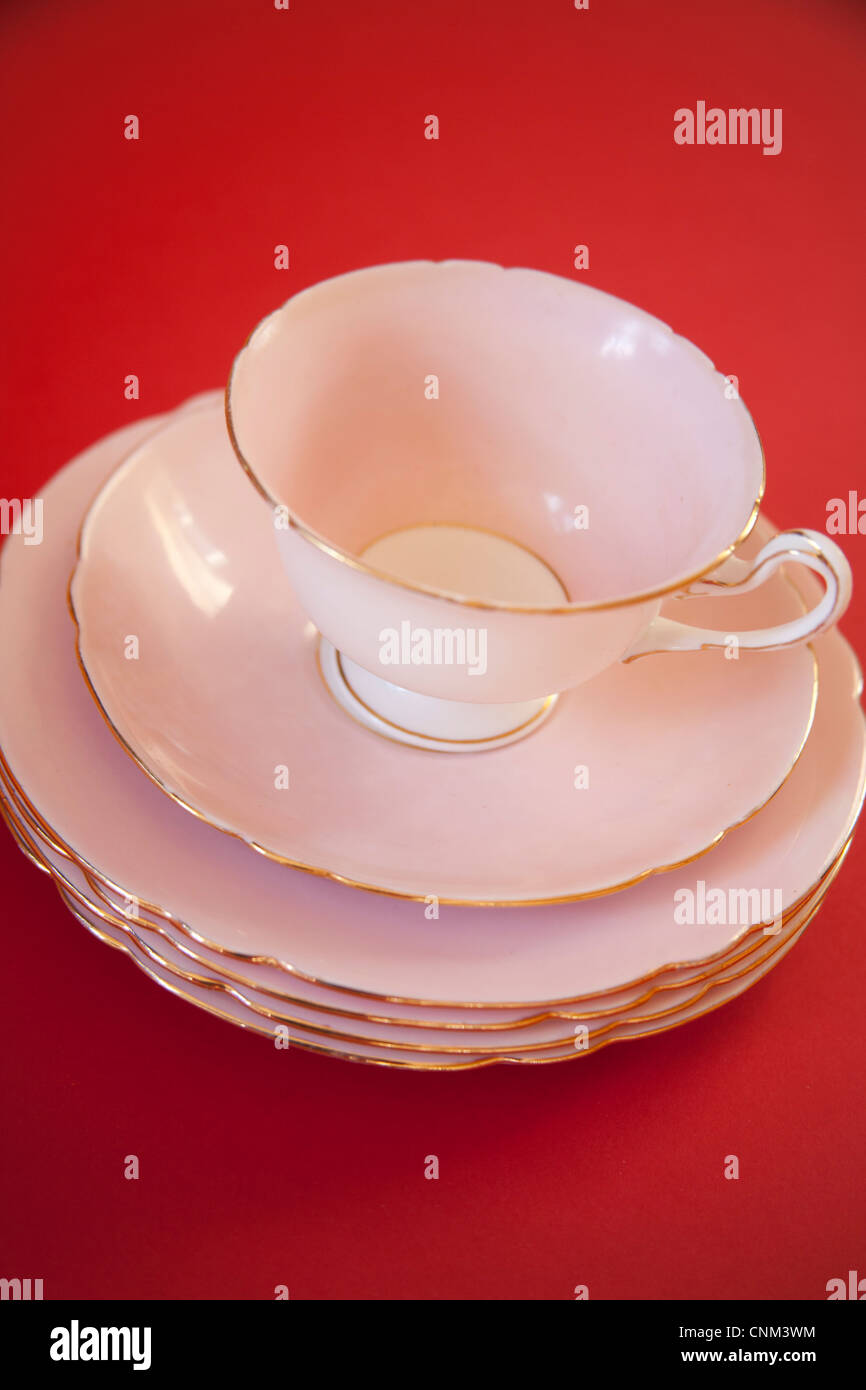 Rosa cina tazza da caffè con piattino e piastre con rivestimento in oro su uno sfondo rosso Foto Stock