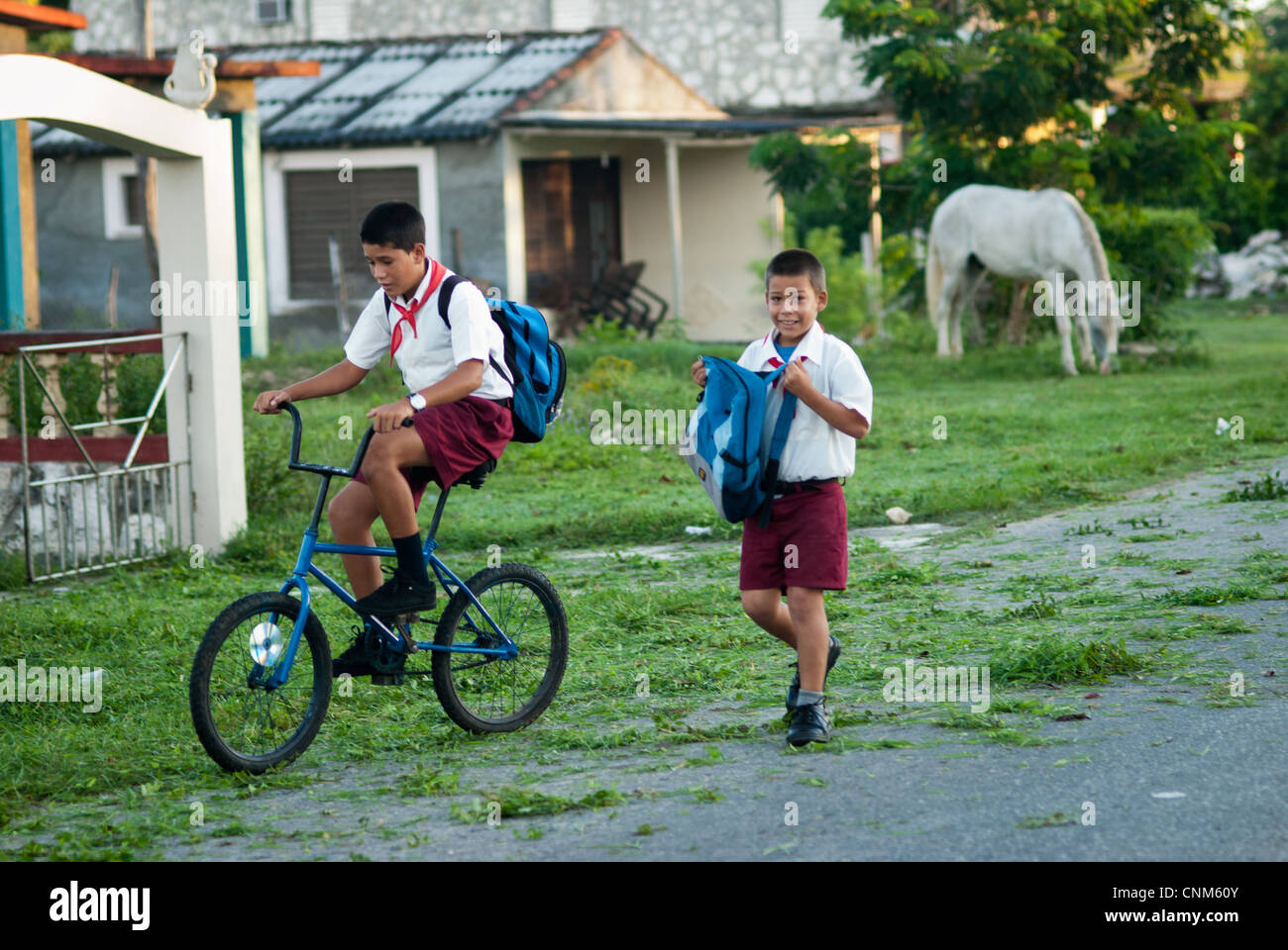 Cuban Boys su una strada per la scuola che indossano le loro uniformi, uno è in sella ad una bicicletta e uno è a piedi e sorridente Foto Stock