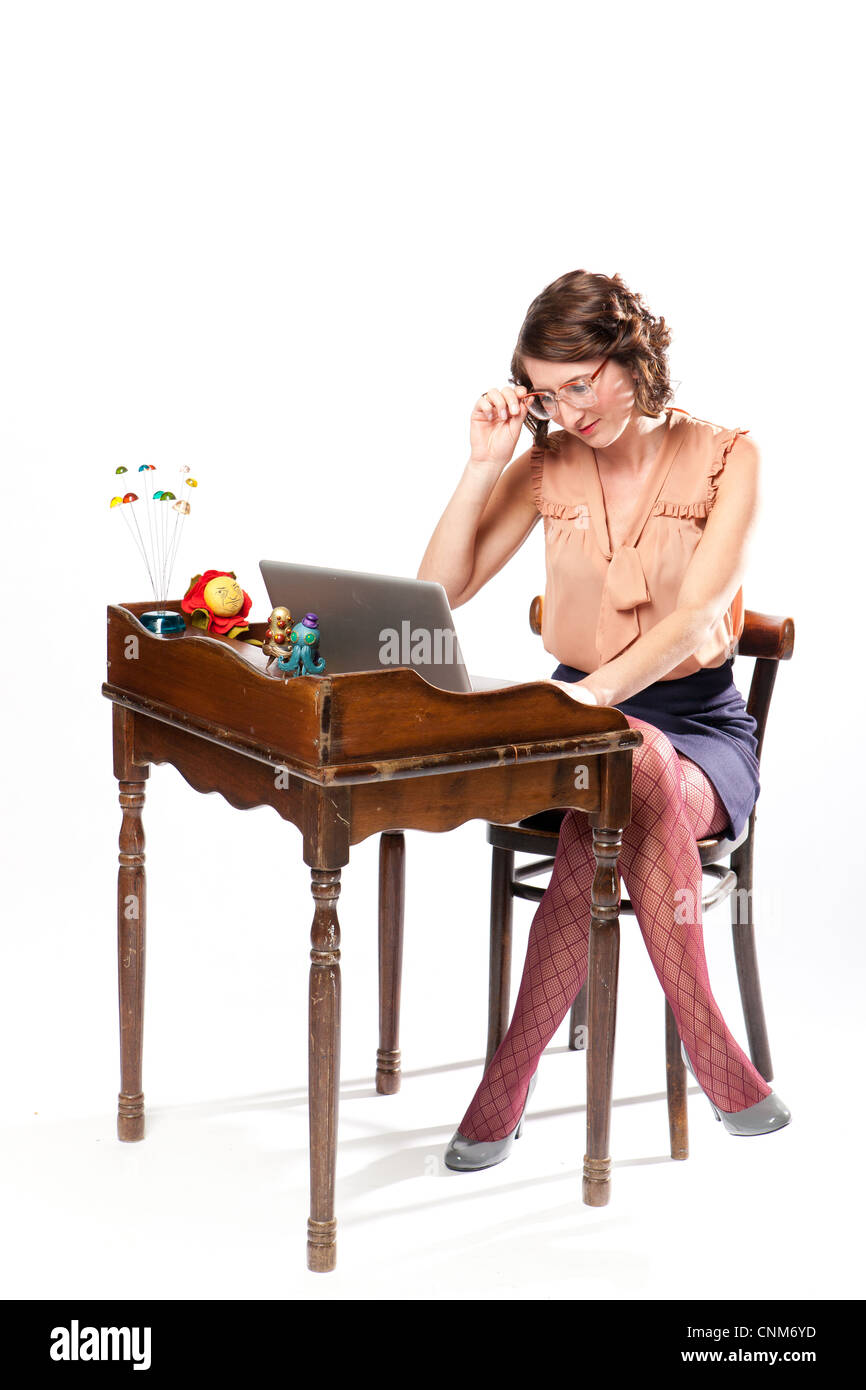 Una donna in abiti retrò si trova a lavorare su un computer presso un banco vintage. Foto Stock