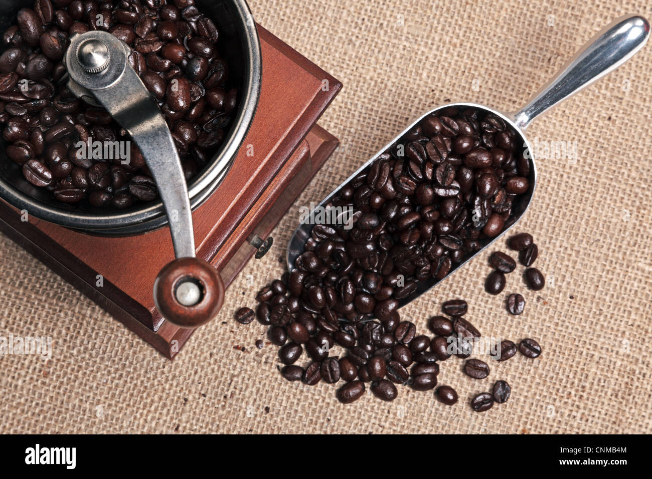 Foto di un azionato a mano tradizionale macinino da caffè con un cucchiaio pieno di chicchi di Arabica su un sfondo di Hesse. Foto Stock