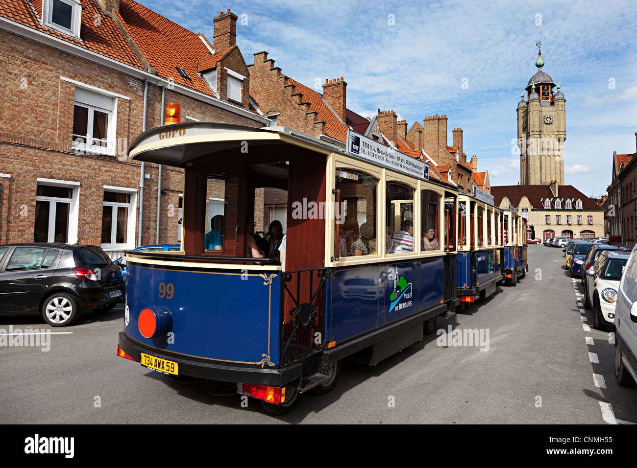 Visite turistiche Road train nelle strade di Bergues con torre campanaria in distanza, Nord, Francia Foto Stock