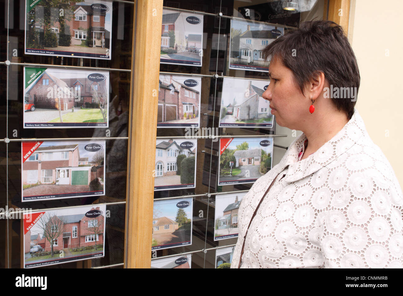 Donna che guarda immobile case in vendita in un agenti immobiliari finestra in Inghilterra, Regno Unito Foto Stock