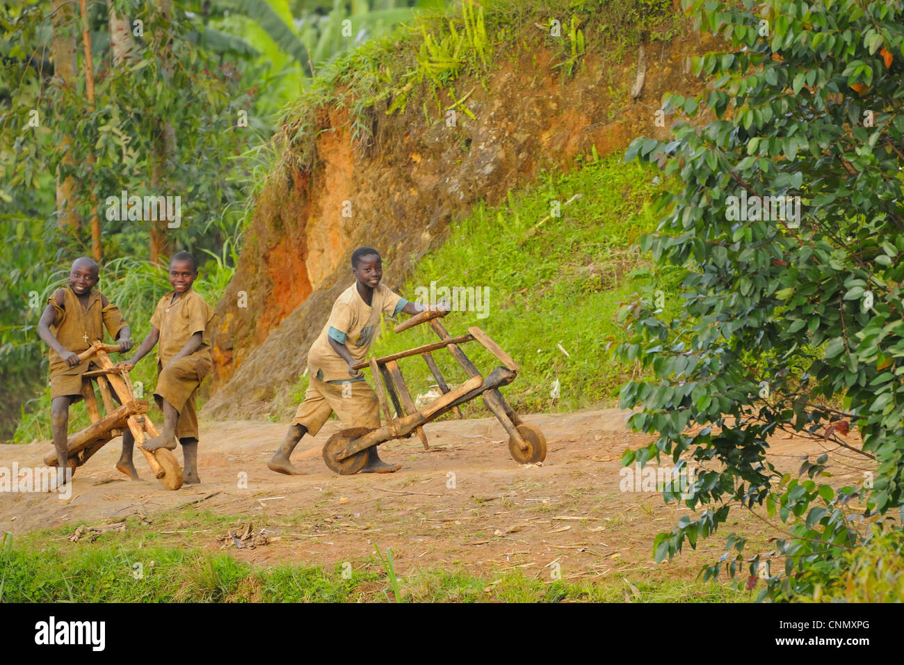 Bambini che giocano con in legno che le biciclette in pista a bordo della foresta di Nyungwe N.P., Ruanda, marzo Foto Stock