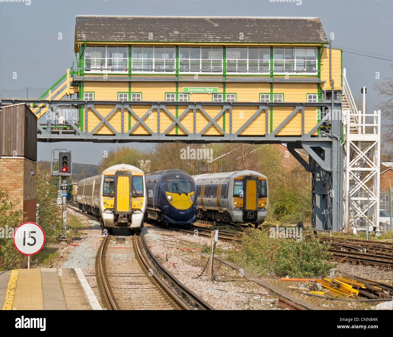 Giavellotto treno ad alta velocità che passa il treno più lento a Canterbury West Station passando sotto il recentemente ridipinto gantry casella segnale. Foto Stock