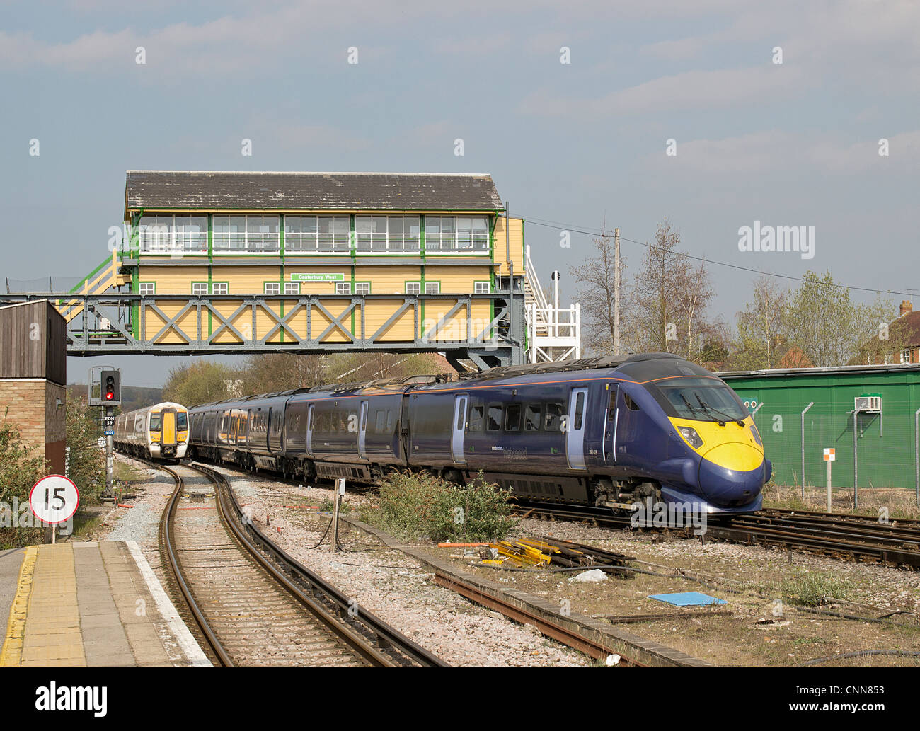 Giavellotto treno ad alta velocità che passa il treno più lento a Canterbury West Station passando sotto il recentemente ridipinto gantry casella segnale. Foto Stock