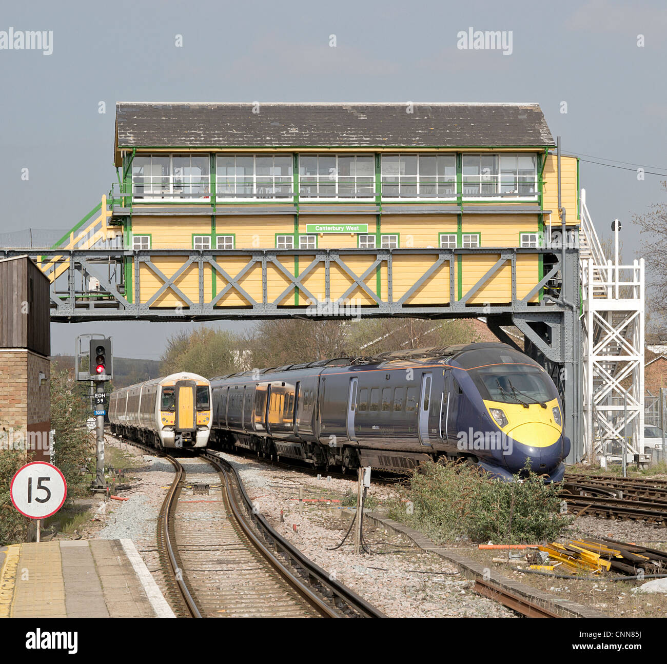 Giavellotto treno ad alta velocità che passa il treno più lento a Canterbury West Station passando sotto il recentemente ridipinto gantry casella segnale. Foto Stock