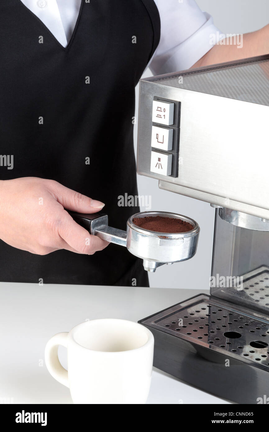 Foto di un barista mettendo un porta-filtro pieno di caffè appena macinato in una macchina per caffè espresso. Foto Stock