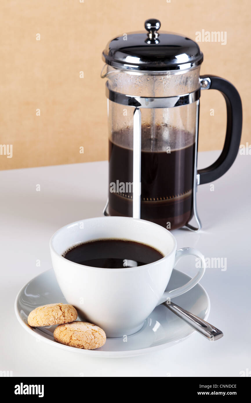 Foto di una tazza di caffè con amaretti sul piattino e un cafetiere piena di caffè appena fatto. Foto Stock